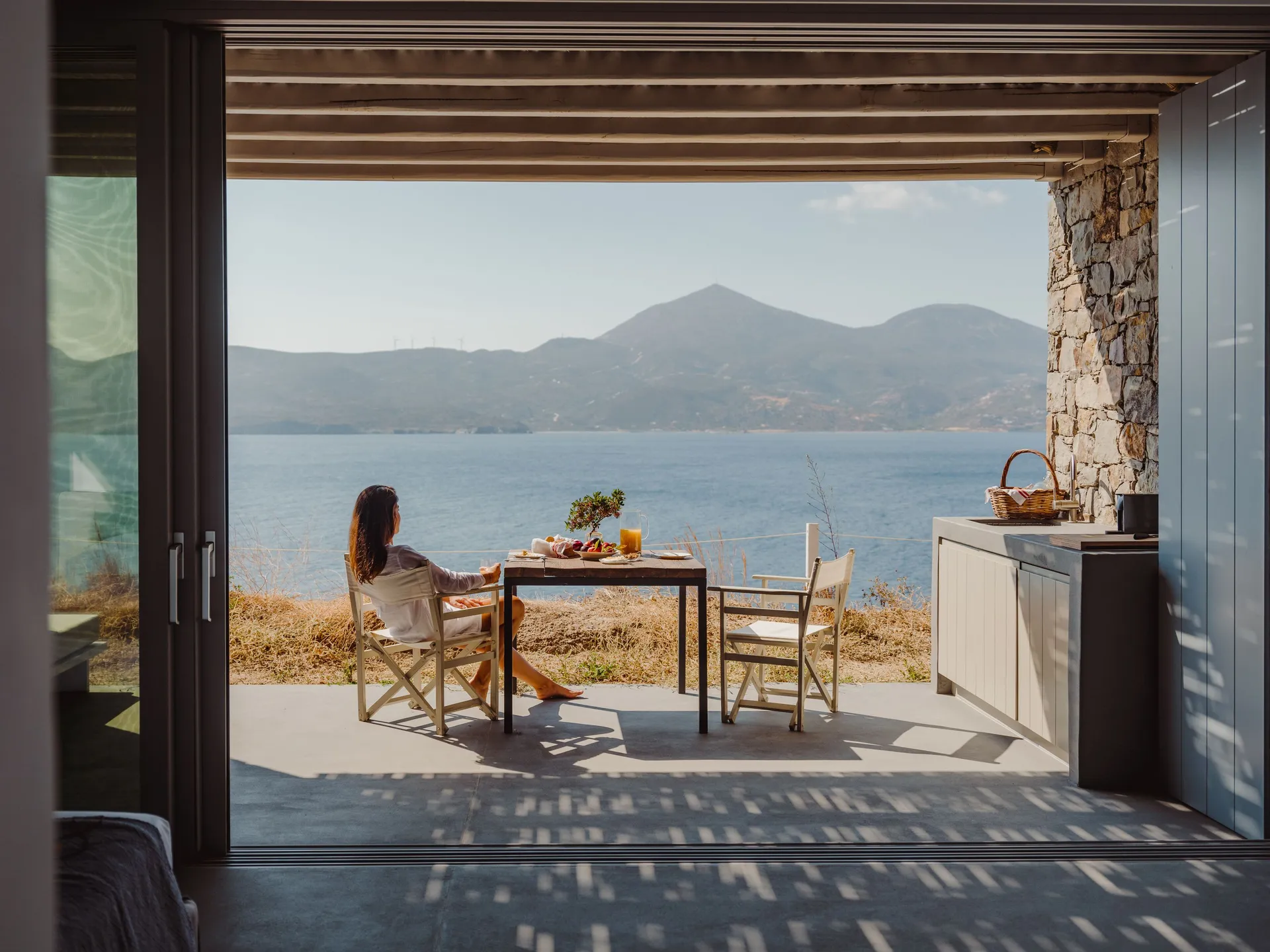 Woman relaxing at a table with mountain and sea view.