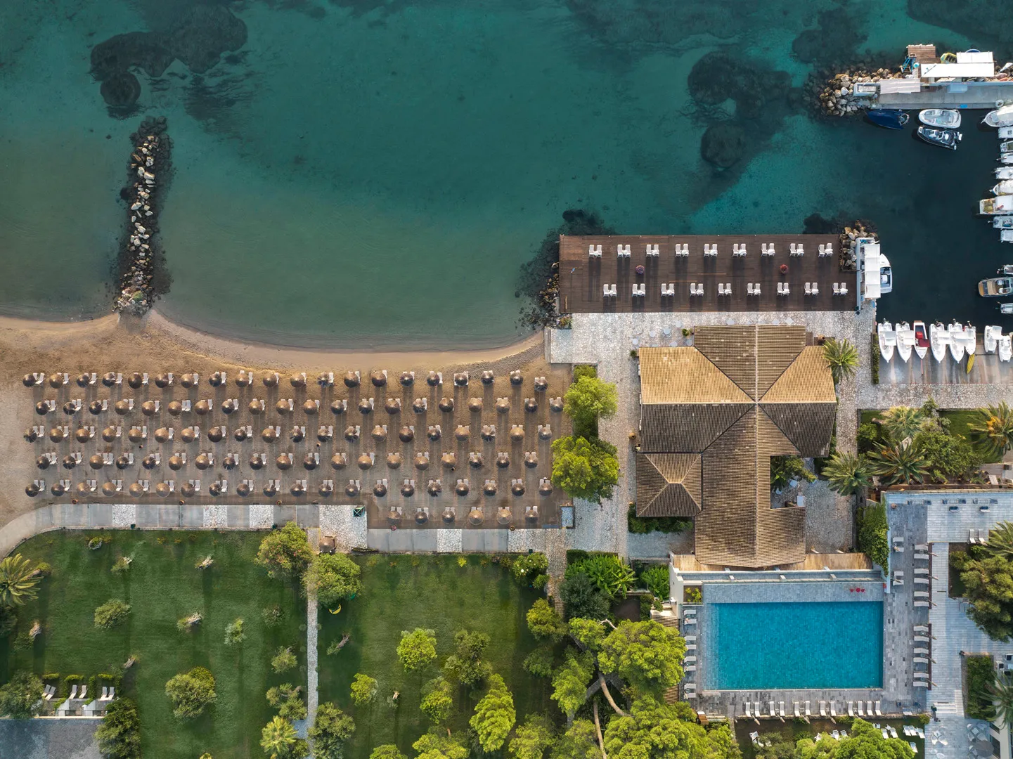 Aerial view of a beach resort with umbrellas, pool, and green lawn.