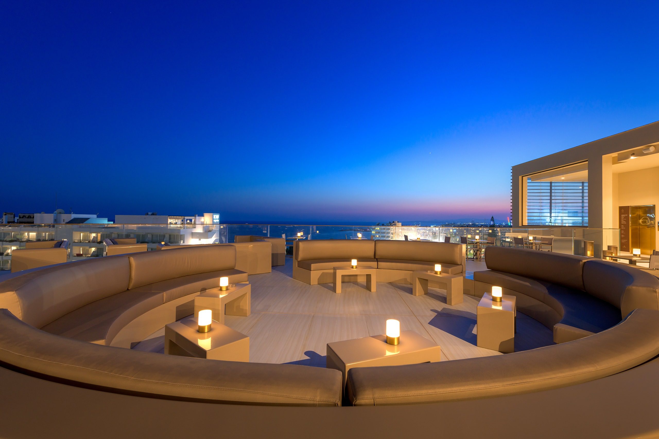 Luxury rooftop lounge with panoramic city and ocean views at dusk.