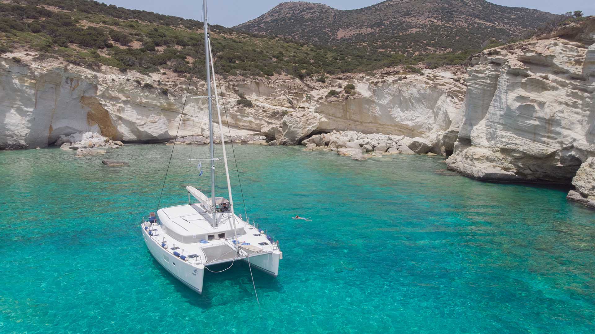 A white catamaran anchored in crystal-clear turquoise waters near rocky shores.