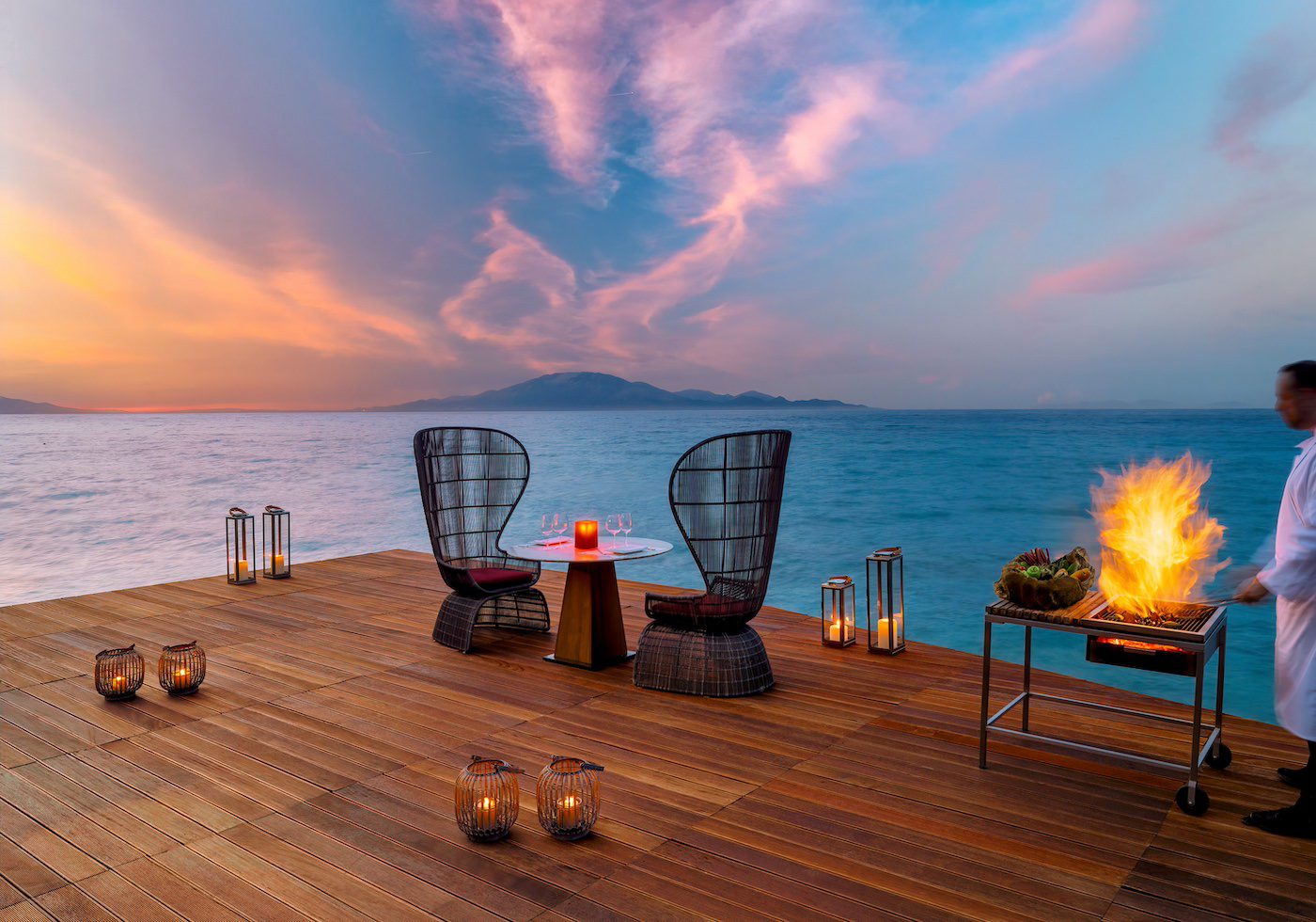 Romantic sunset seating by the ocean with cozy chairs and candles.