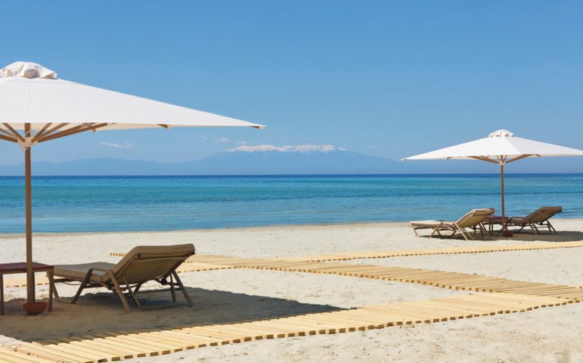 Beach chairs neatly arranged on a sunny sandy beach with umbrellas and clear blue sea.
