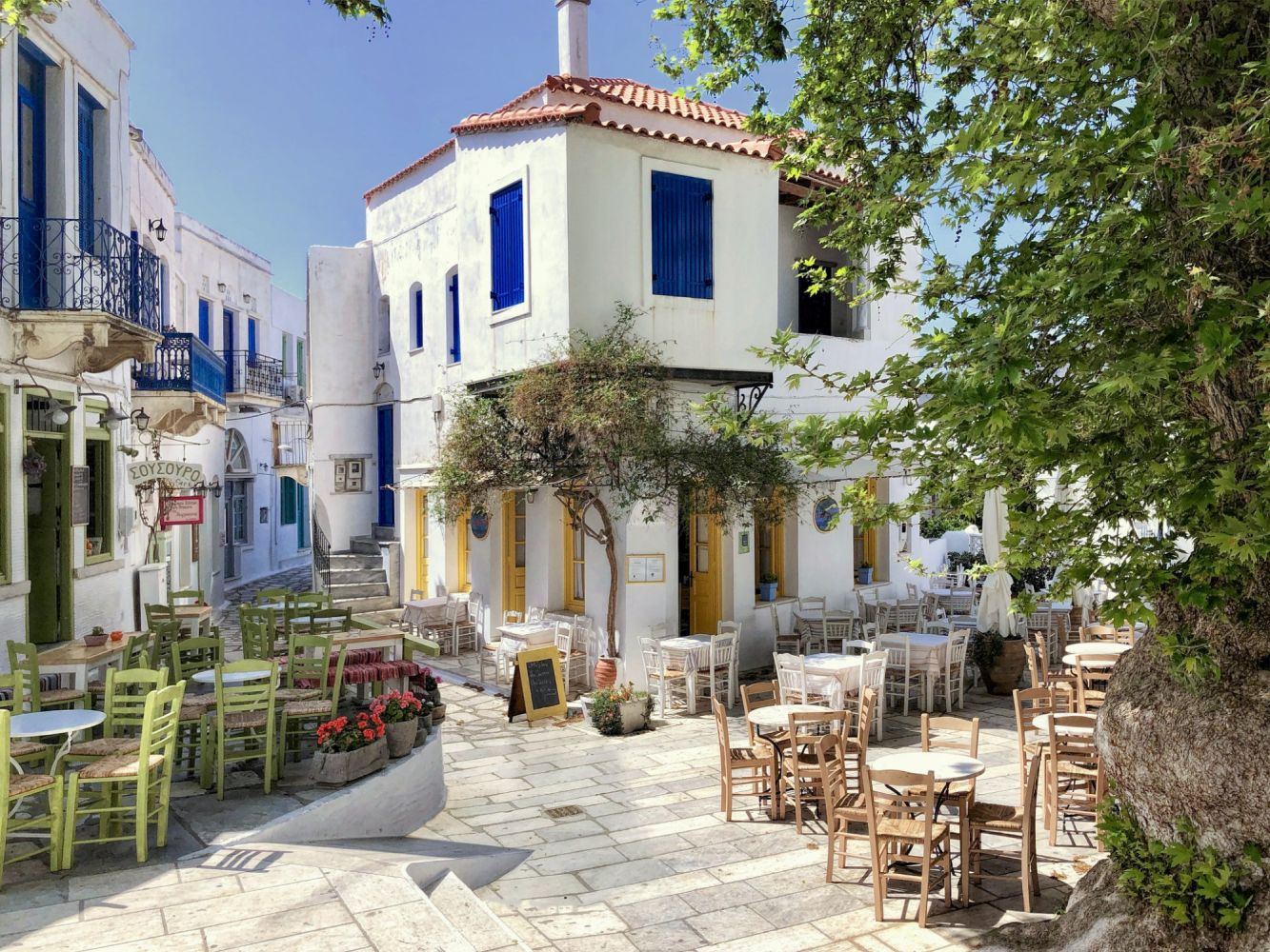 Charming outdoor cafe with wooden chairs in a sunny Mediterranean village.