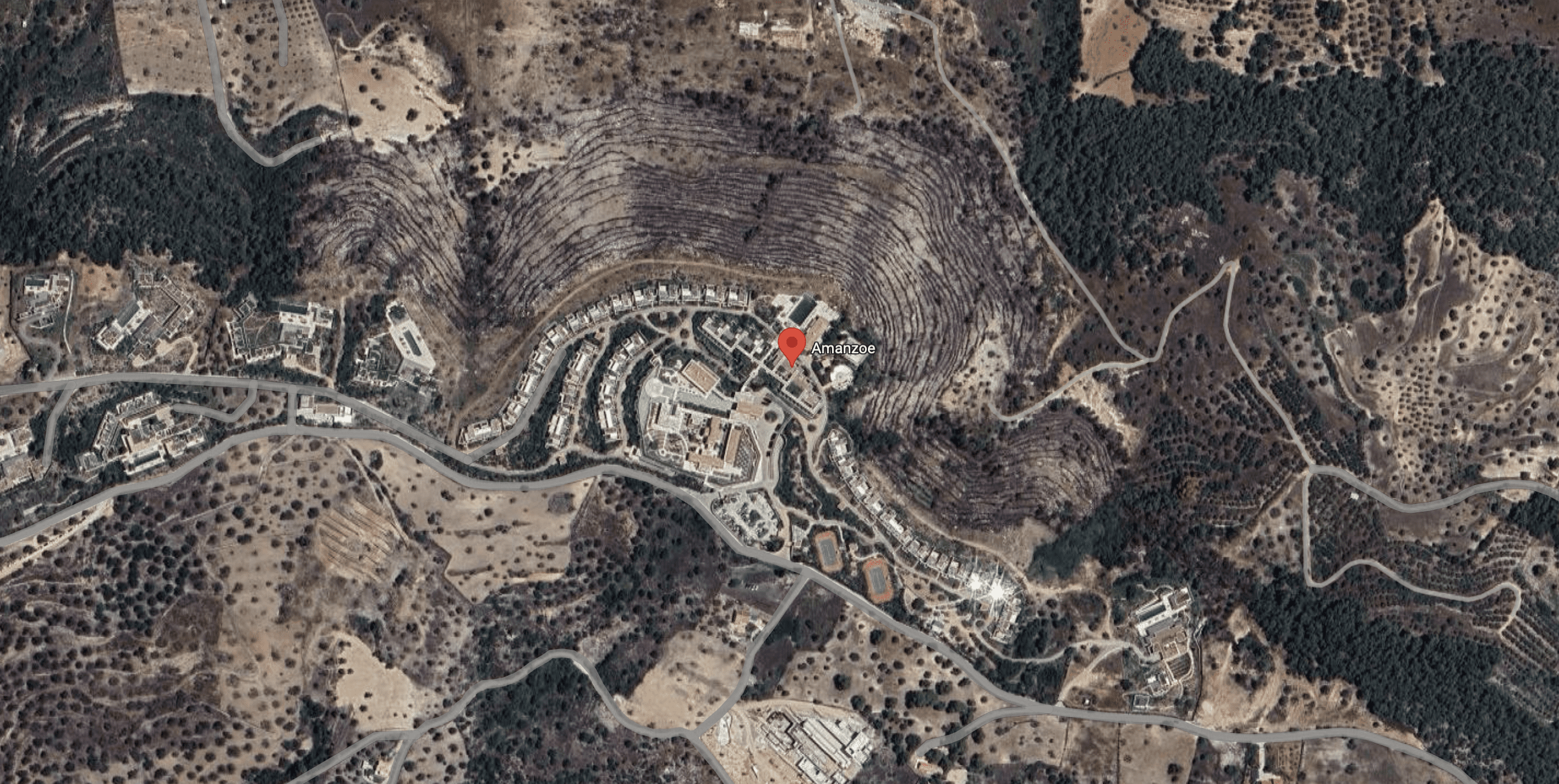 A satellite view of a residential area surrounded by dry terrain and sparse vegetation.
