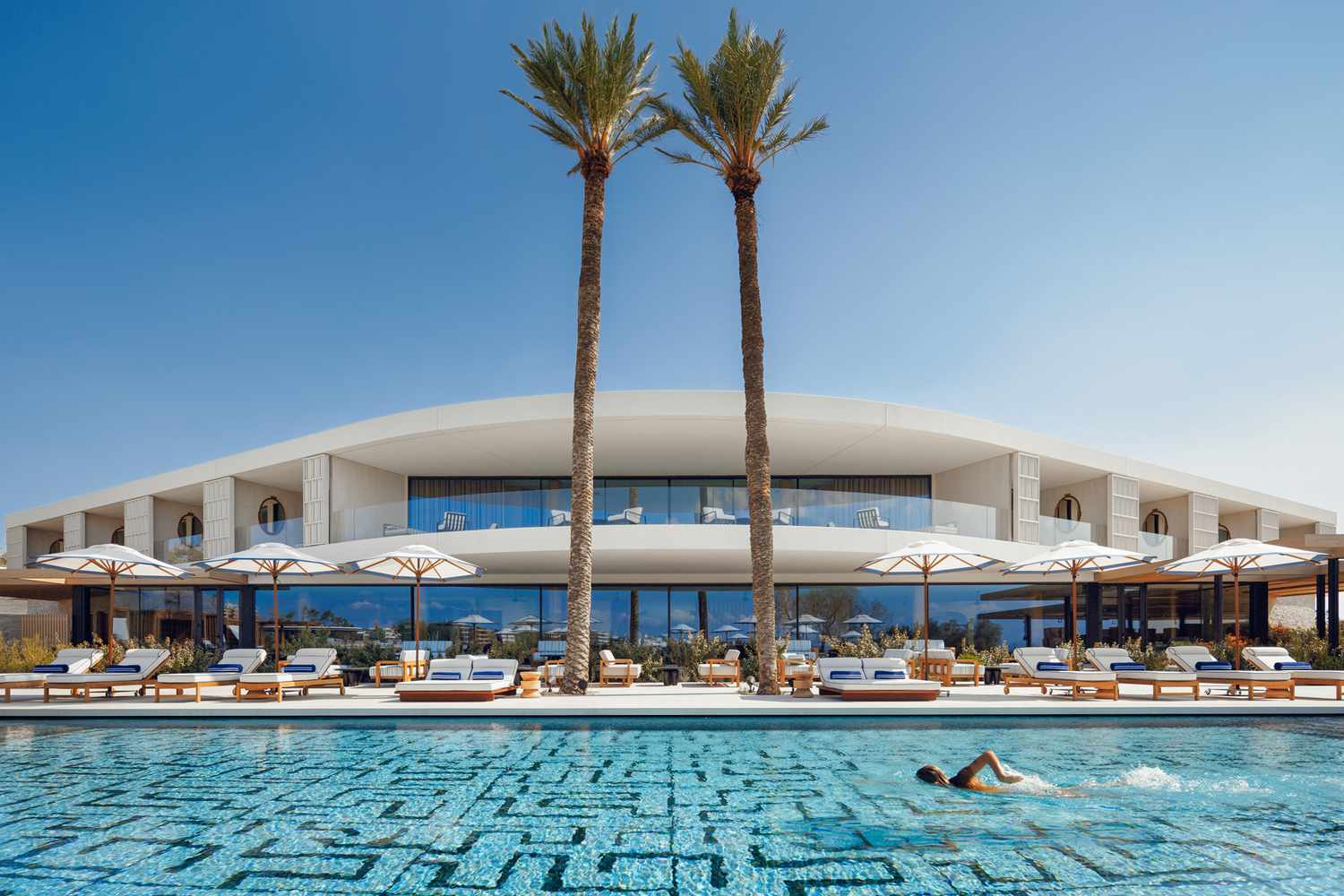 Modern poolside resort with tall palm trees and a swimmer.