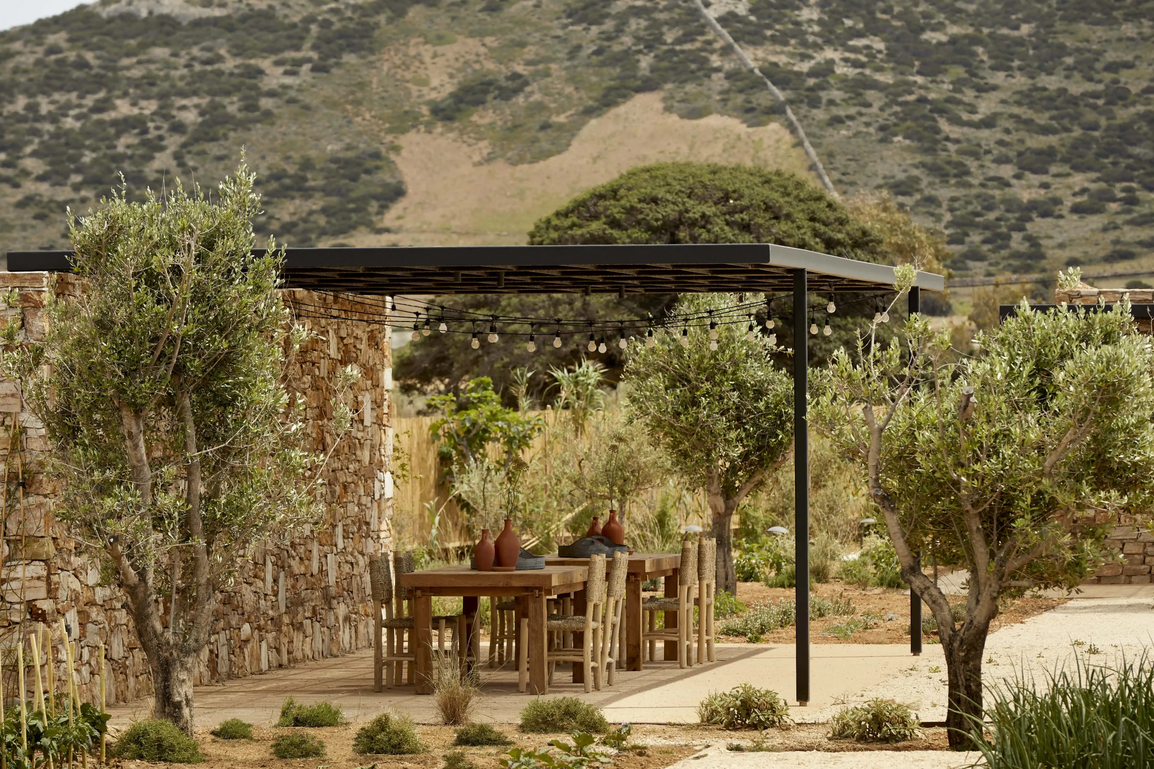 Outdoor dining area with wooden furniture under a pergola in a scenic mountainous setting.