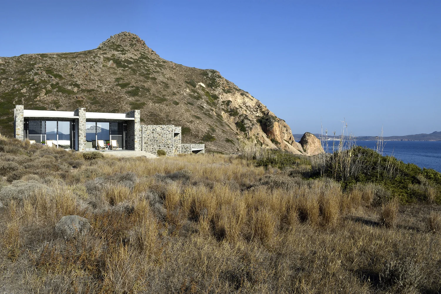 Modern house near rocky hills under a clear blue sky.