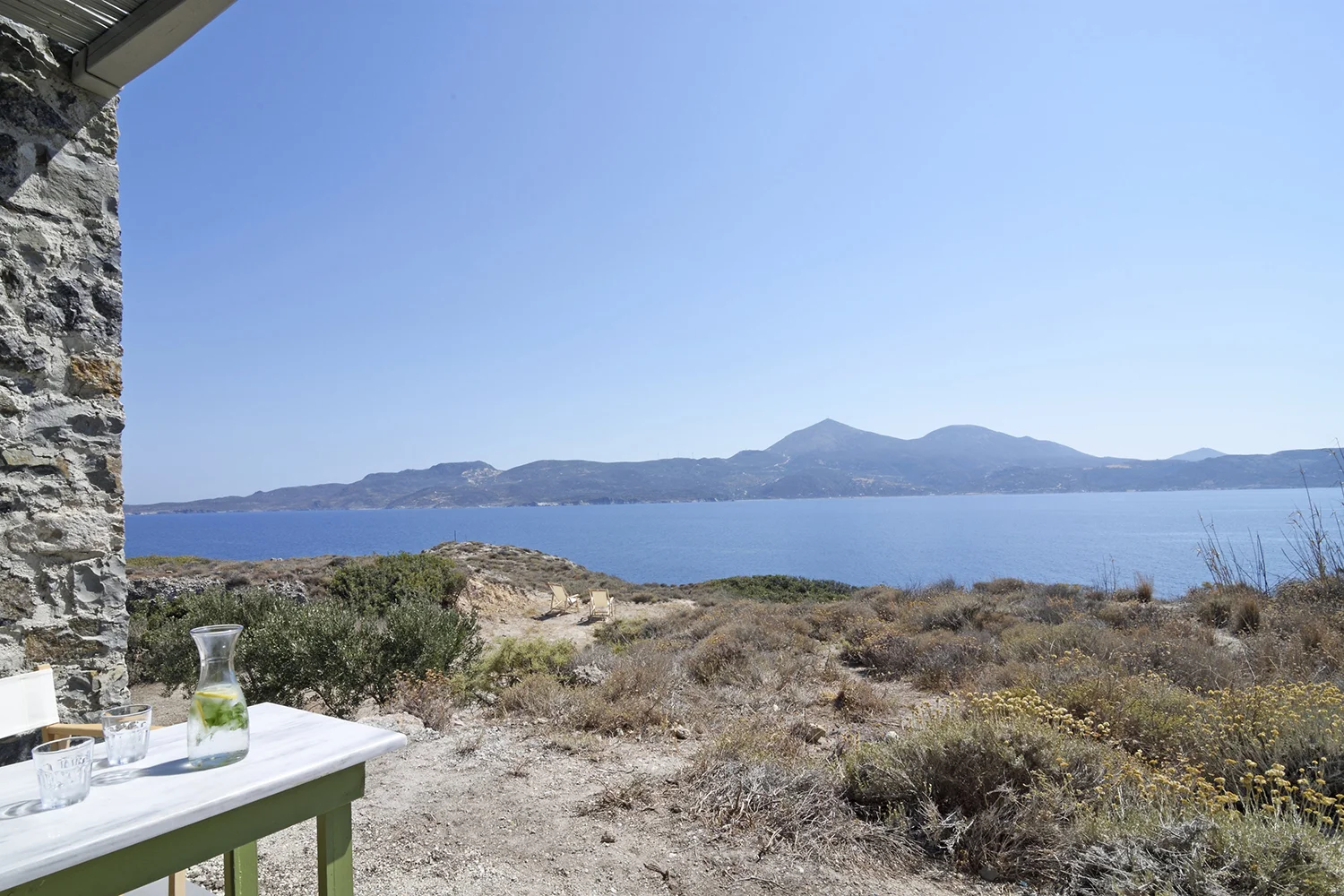A calm coastal view with mountains and clear blue sky.