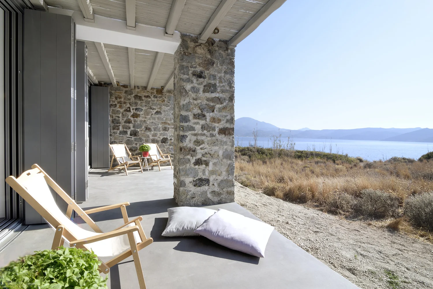 Cozy outdoor seating with cushions on a stone patio overlooking a scenic waterfront.