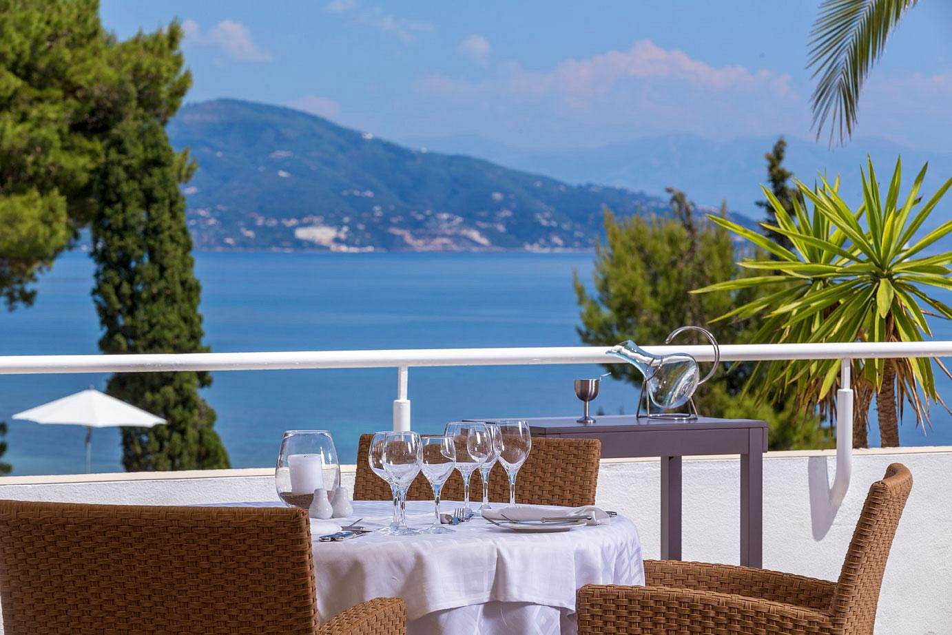 Elegant outdoor dining setup overlooking a calm blue sea and distant hills.
