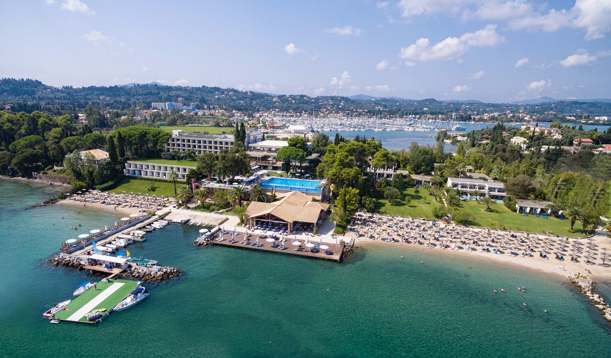 A coastal resort with pools, beach, and clear blue water under a sunny sky.