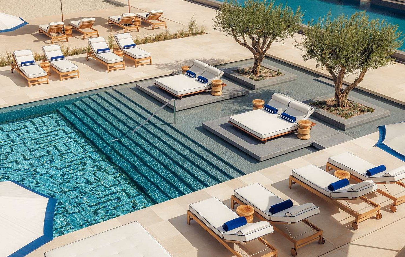 Luxurious poolside beds with blue towels overlooking a serene beach.