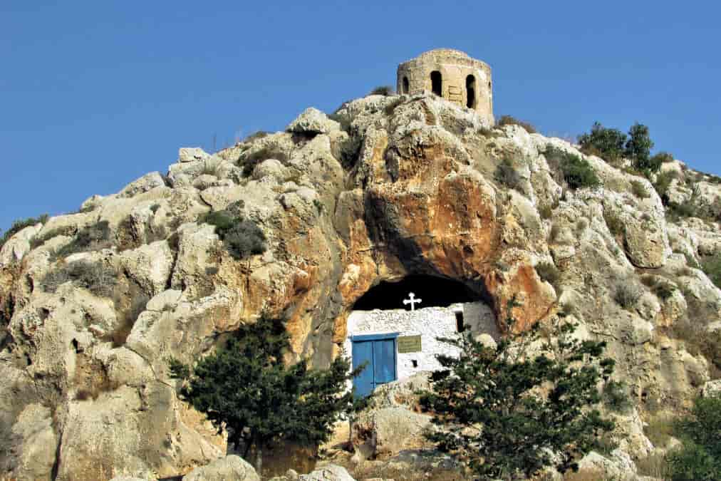 A small white chapel built into a rocky hillside under a clear blue sky.
