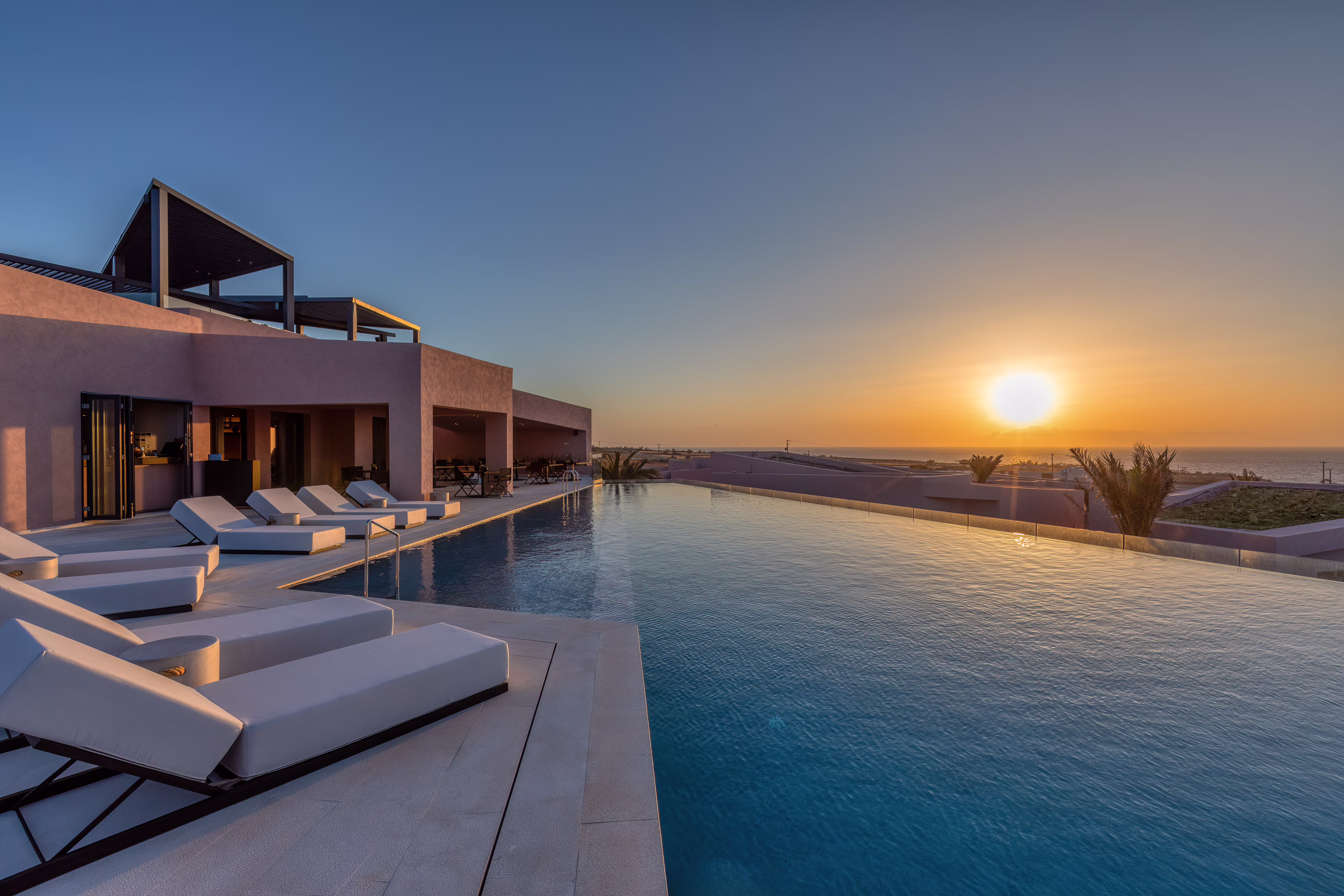 Sunset over a luxurious infinity pool with lounge chairs.