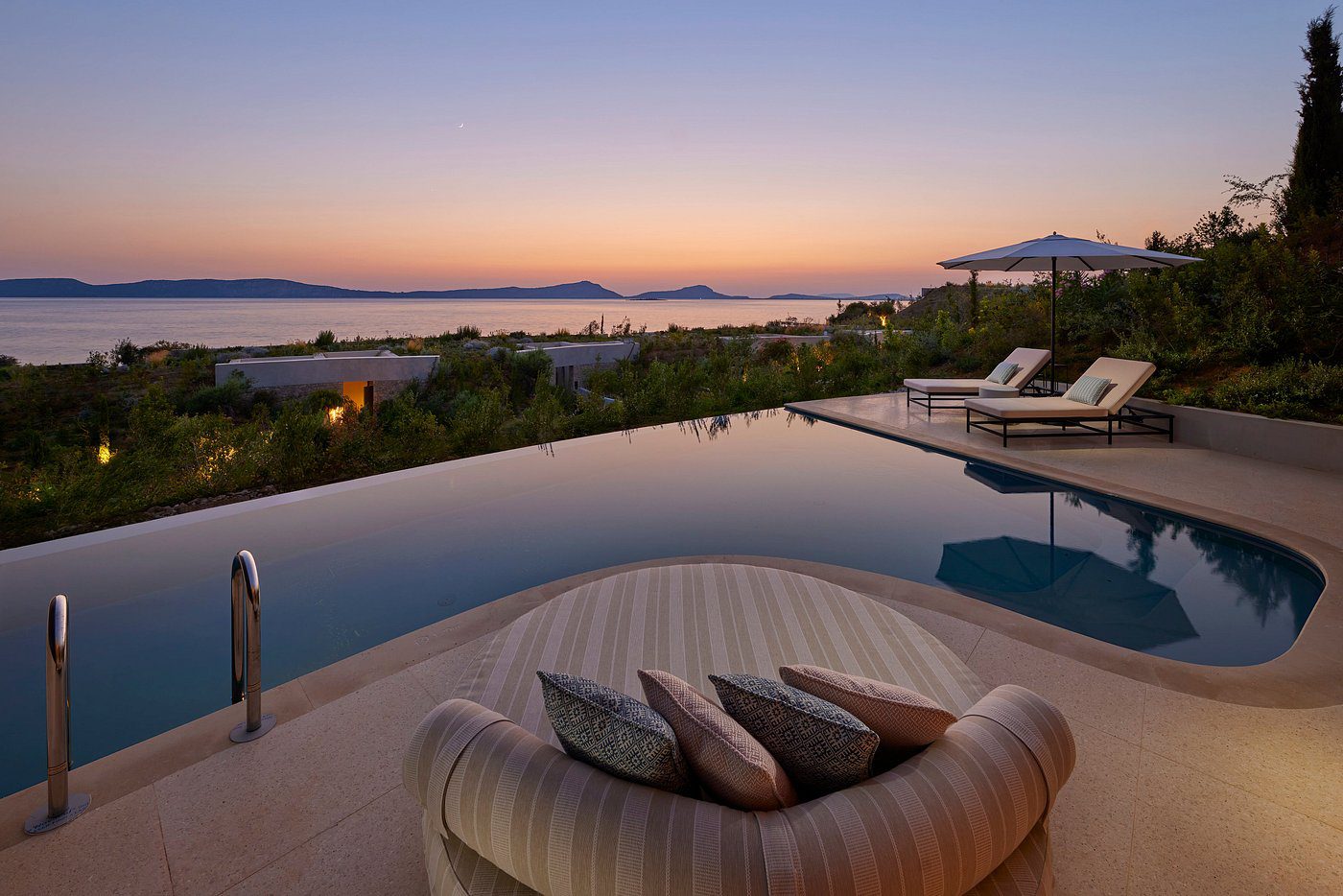 Sunset view over a serene infinity pool with city skyline in the distance.