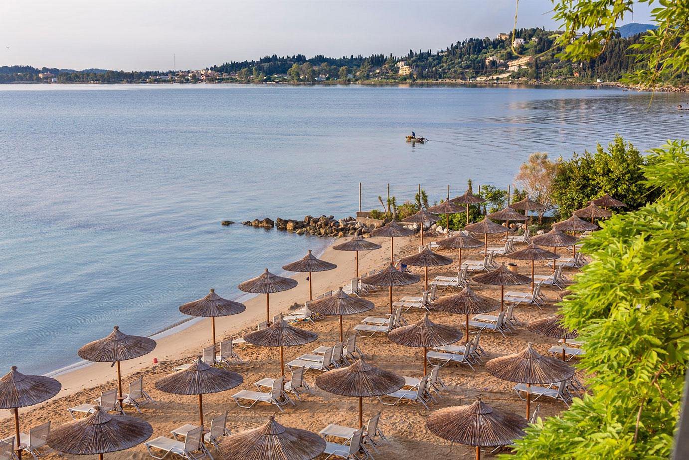 Empty beach umbrellas lined up along a calm shoreline at sunset.