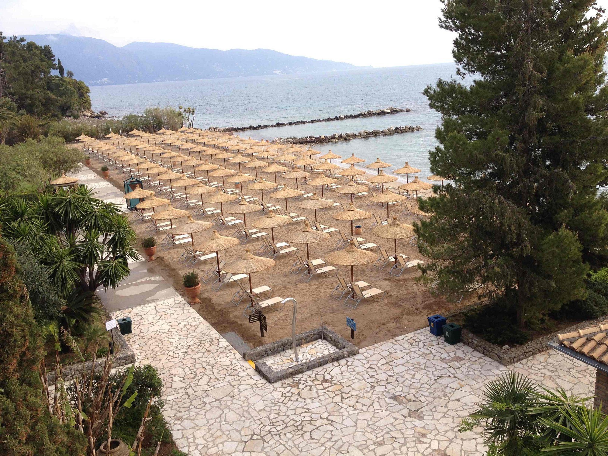 Rows of empty beach sunbeds facing the sea with a pier in the background.