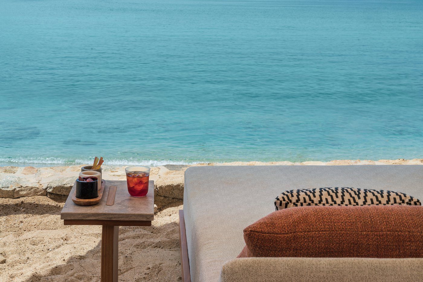 Cozy seaside lounge with drinks and cushions overlooking the ocean.
