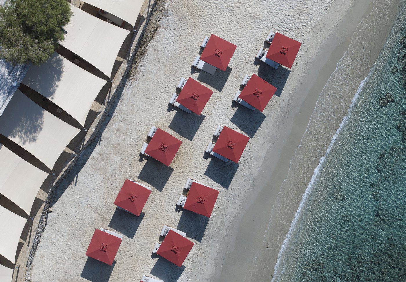 Aerial view of beach umbrellas with red tops arranged neatly by the shore.