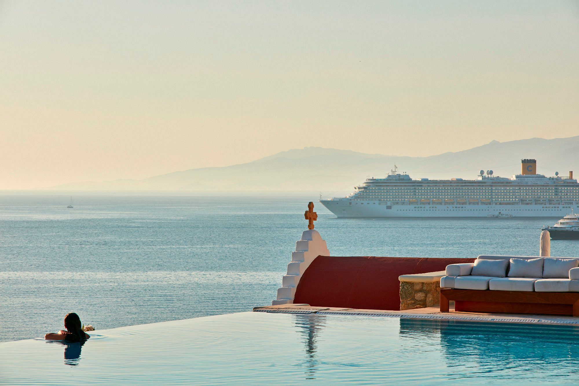 Infinity pool overlooking the sea and distant mountains at sunset.