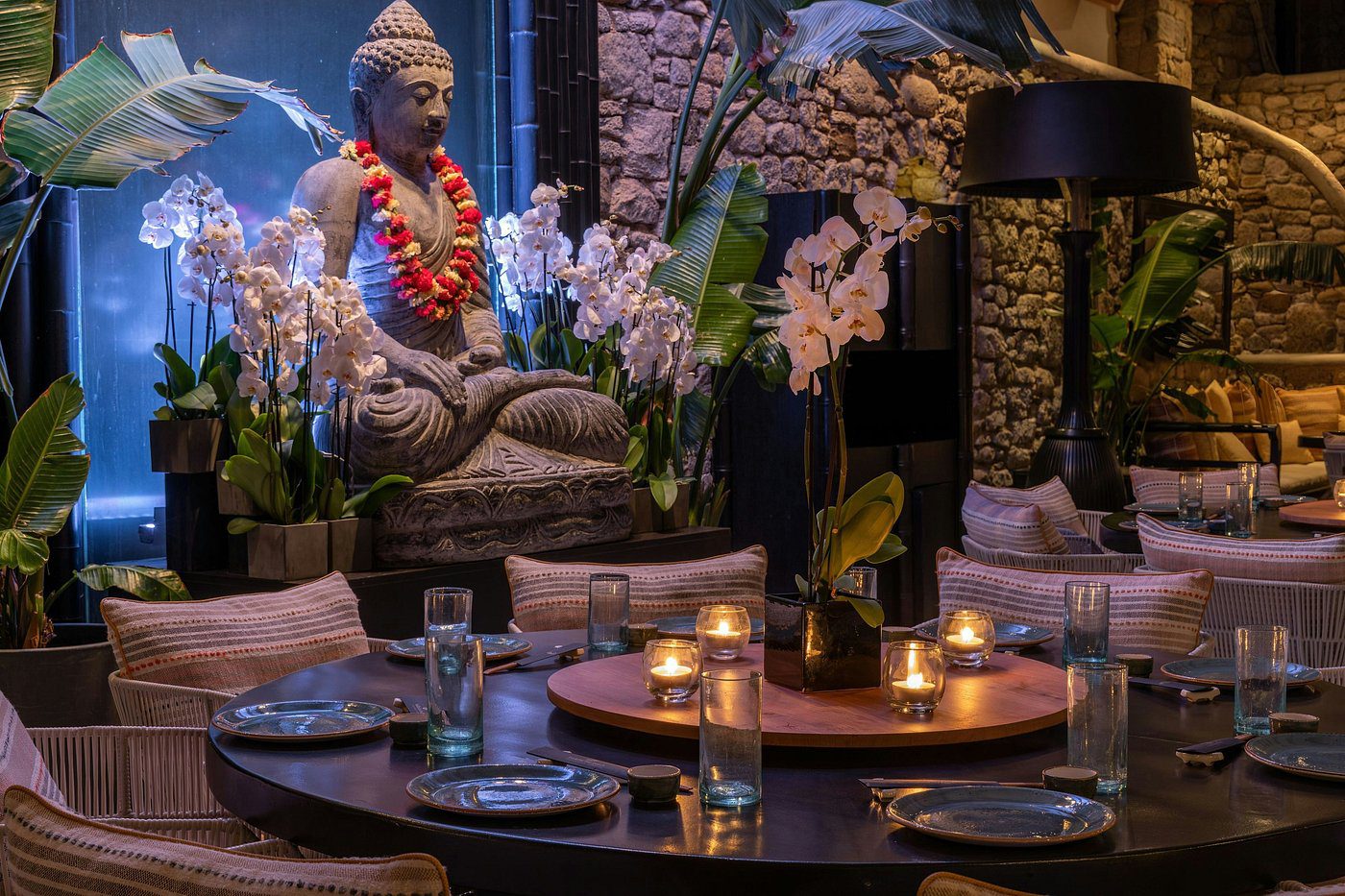 A serene Buddha statue surrounded by candles and orchids in a dimly lit room.