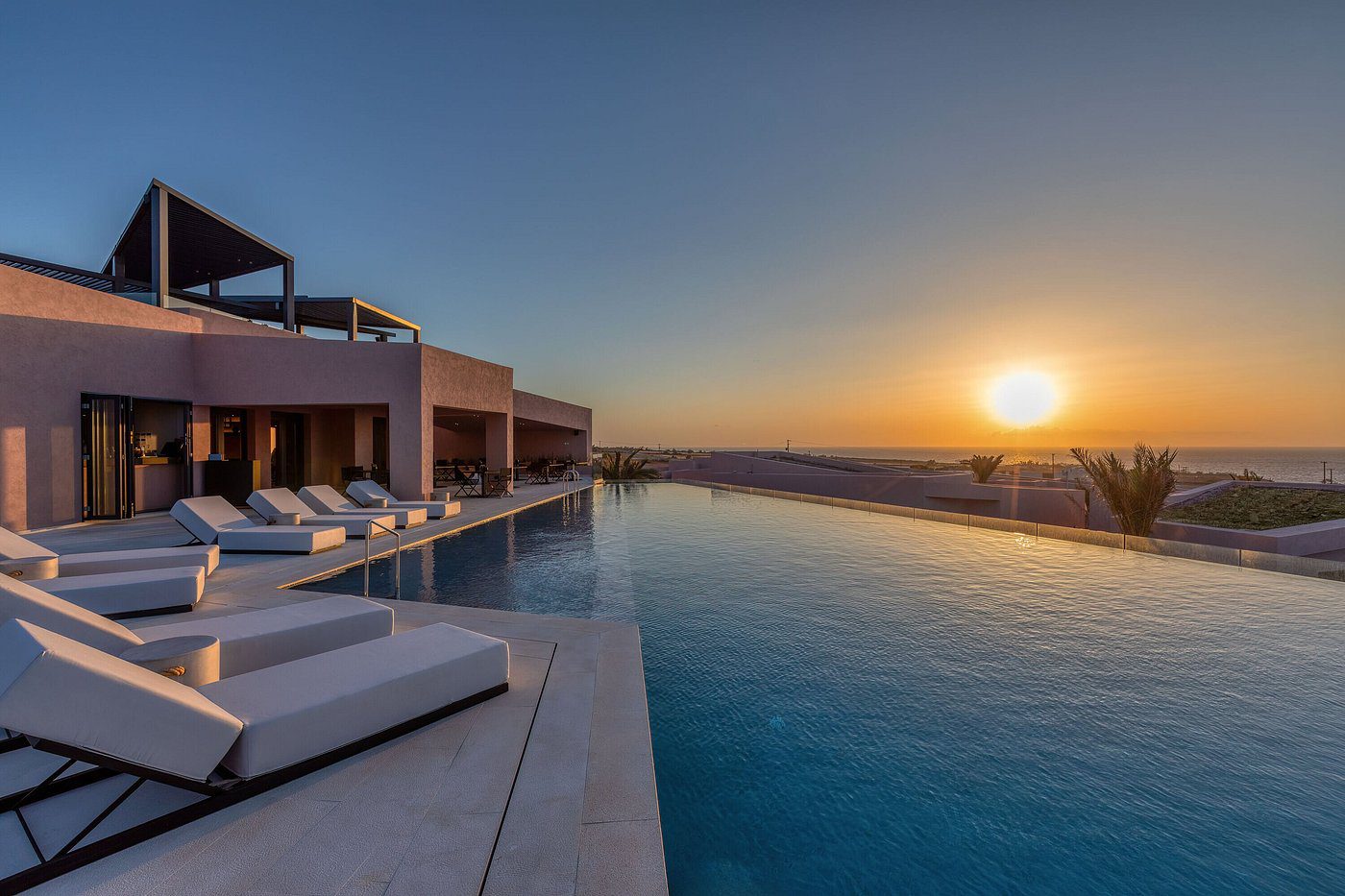 A luxurious poolside at sunset with lounge chairs and clear skies.