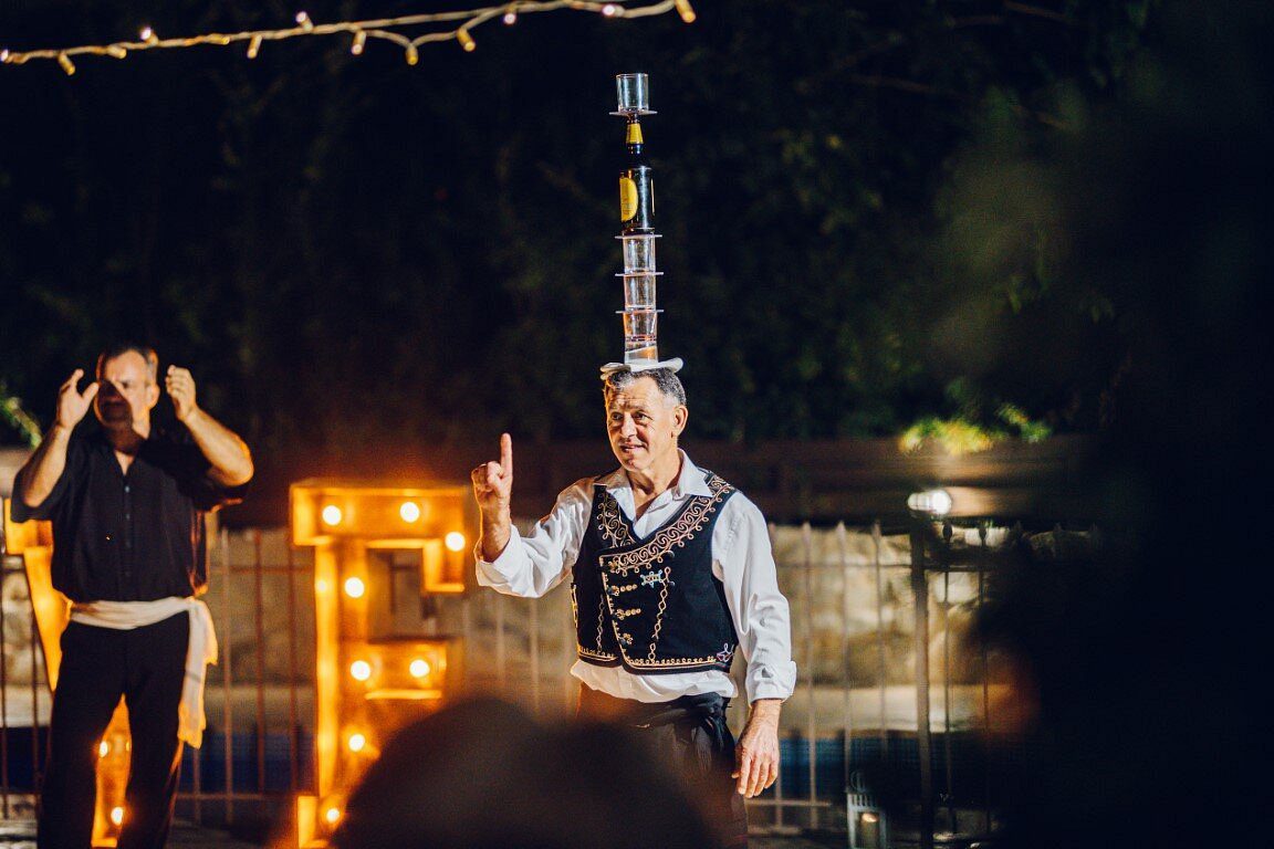 Performer balancing multiple glasses on his head at an outdoor event.