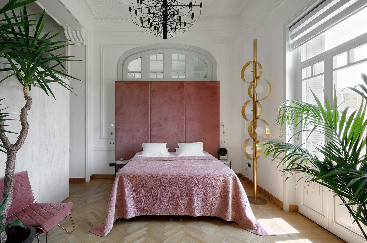 Modern bedroom with a plush pink bed and elegant chandelier.