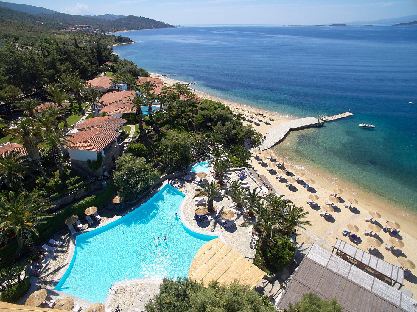 A scenic beach resort with a pool and sun loungers overlooking the sea.