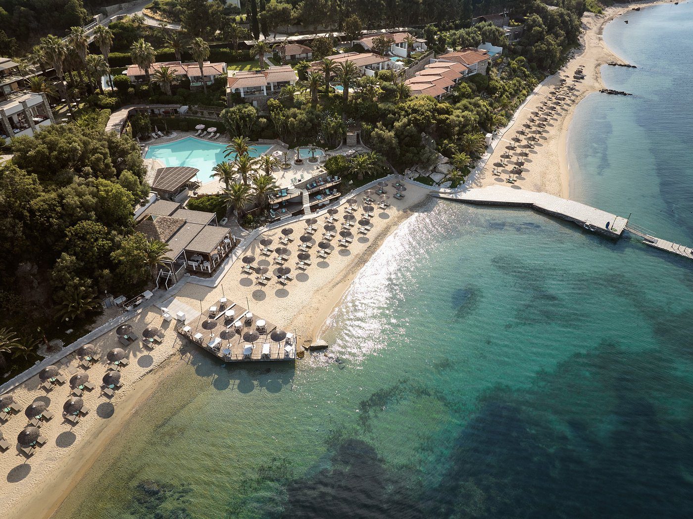 Aerial view of a beach resort with umbrellas and clear turquoise water.
