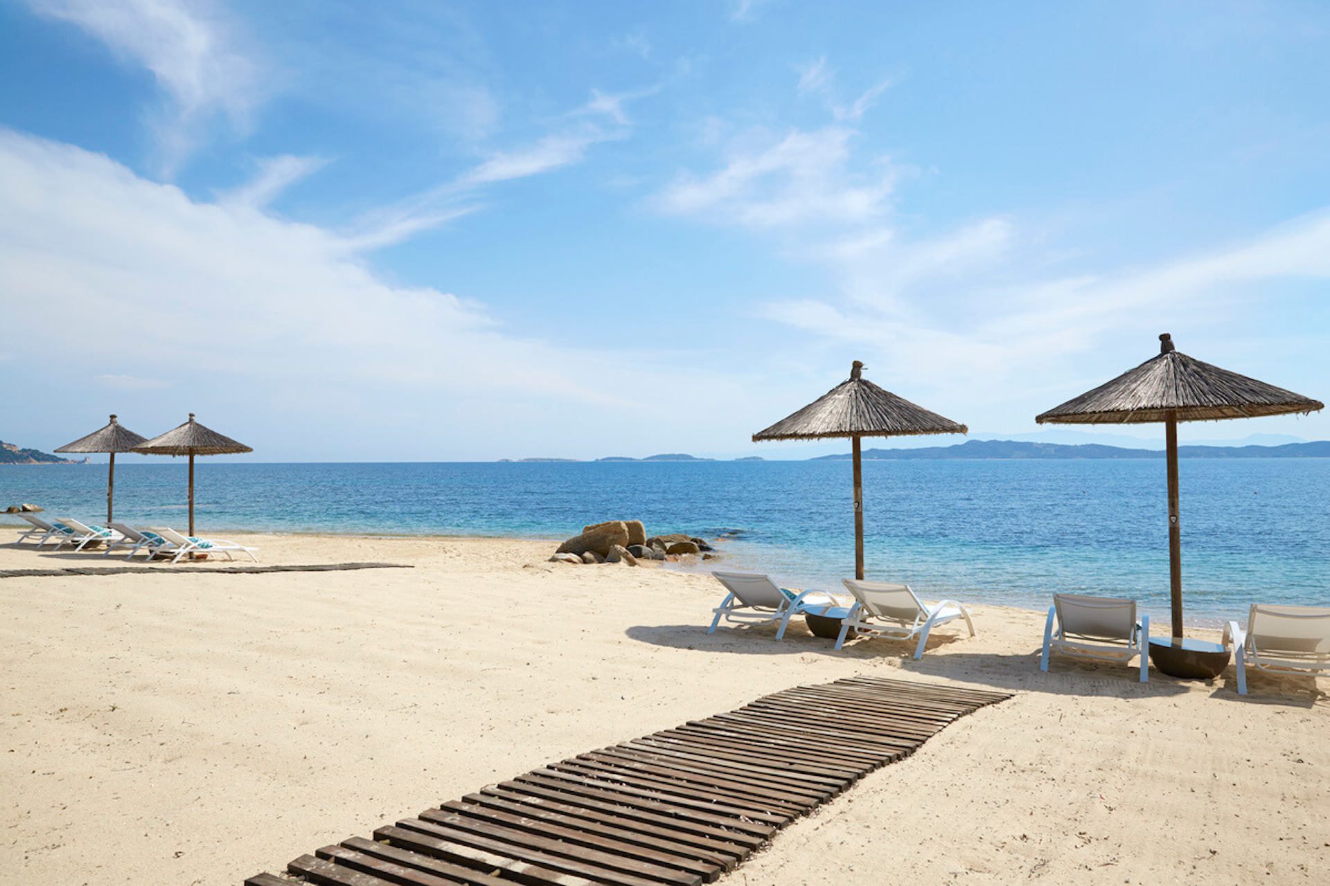 Empty beach chairs under umbrellas on a sunny day by the sea.