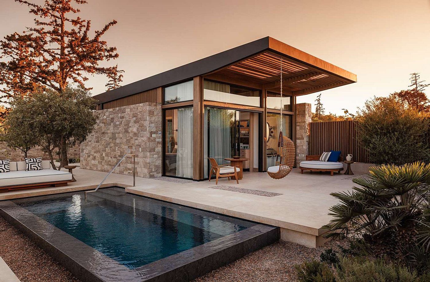 Modern house with large glass walls and a pool at sunset.