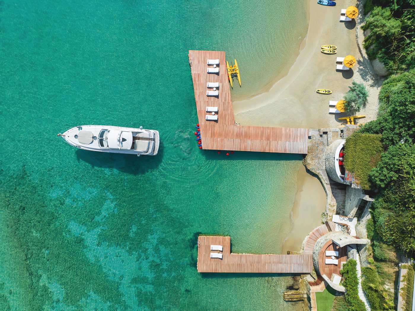 Aerial view of a boat docked near a wooden pier on clear turquoise water.