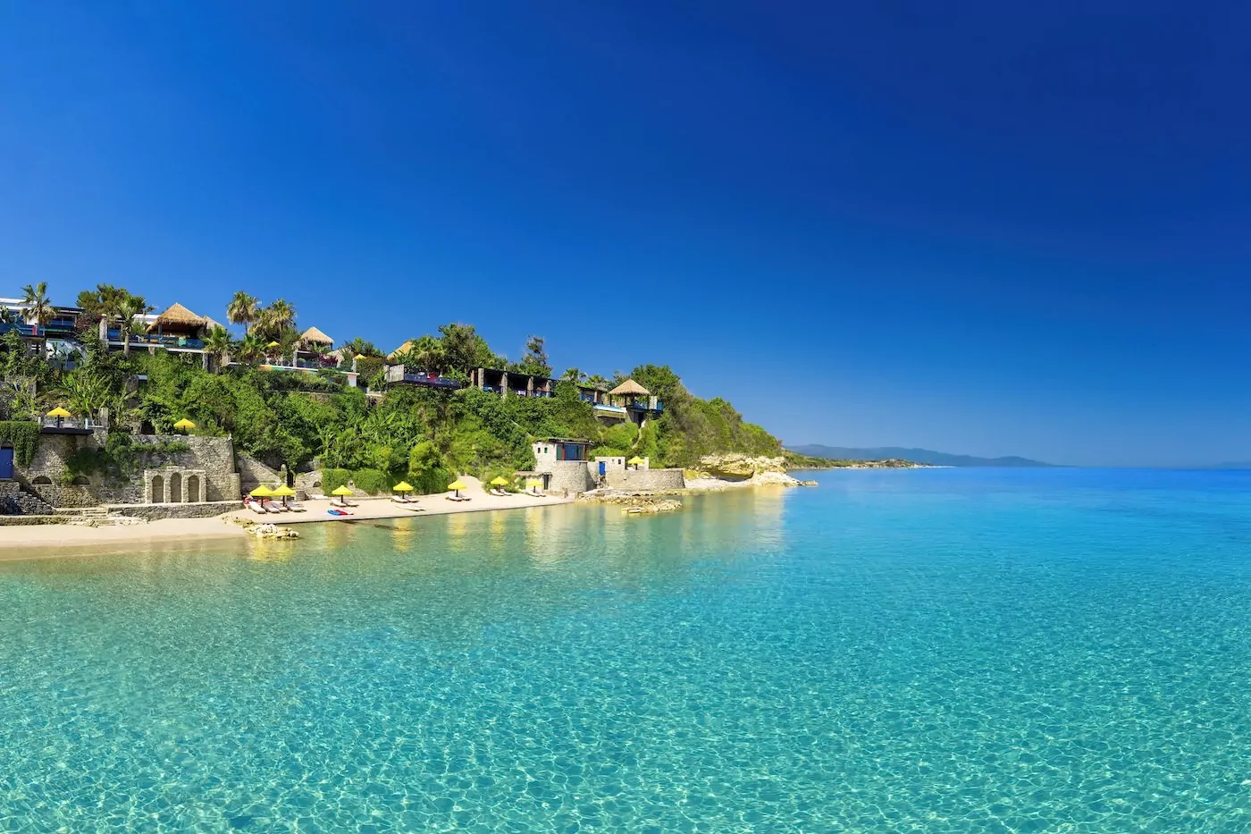 Crystal-clear turquoise water along a tropical beach with lush greenery.
