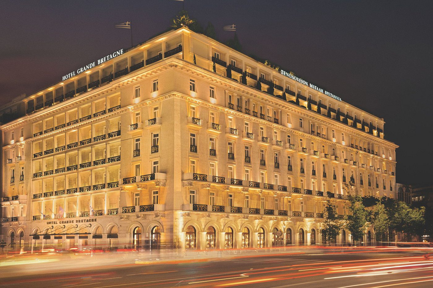 A grand, illuminated historic building at night with light trails from passing cars.