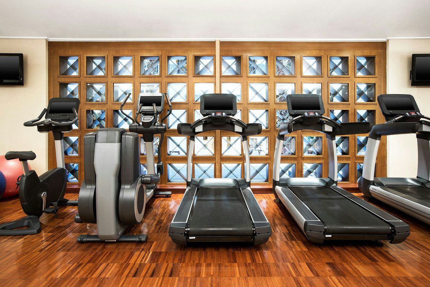 Modern gym with treadmills and exercise bikes in front of a glass brick wall.