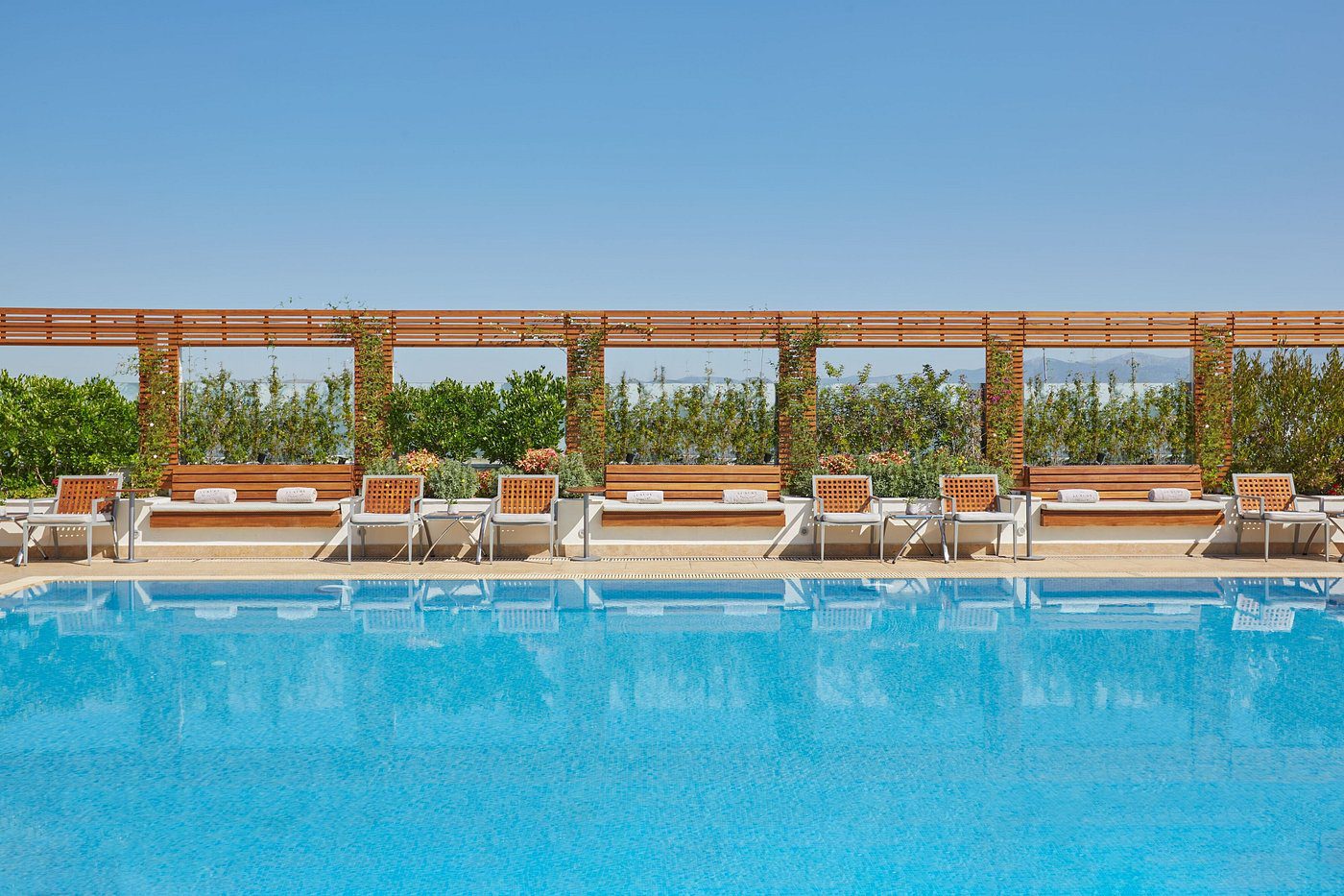 Empty poolside loungers with clear blue water under sunny sky.