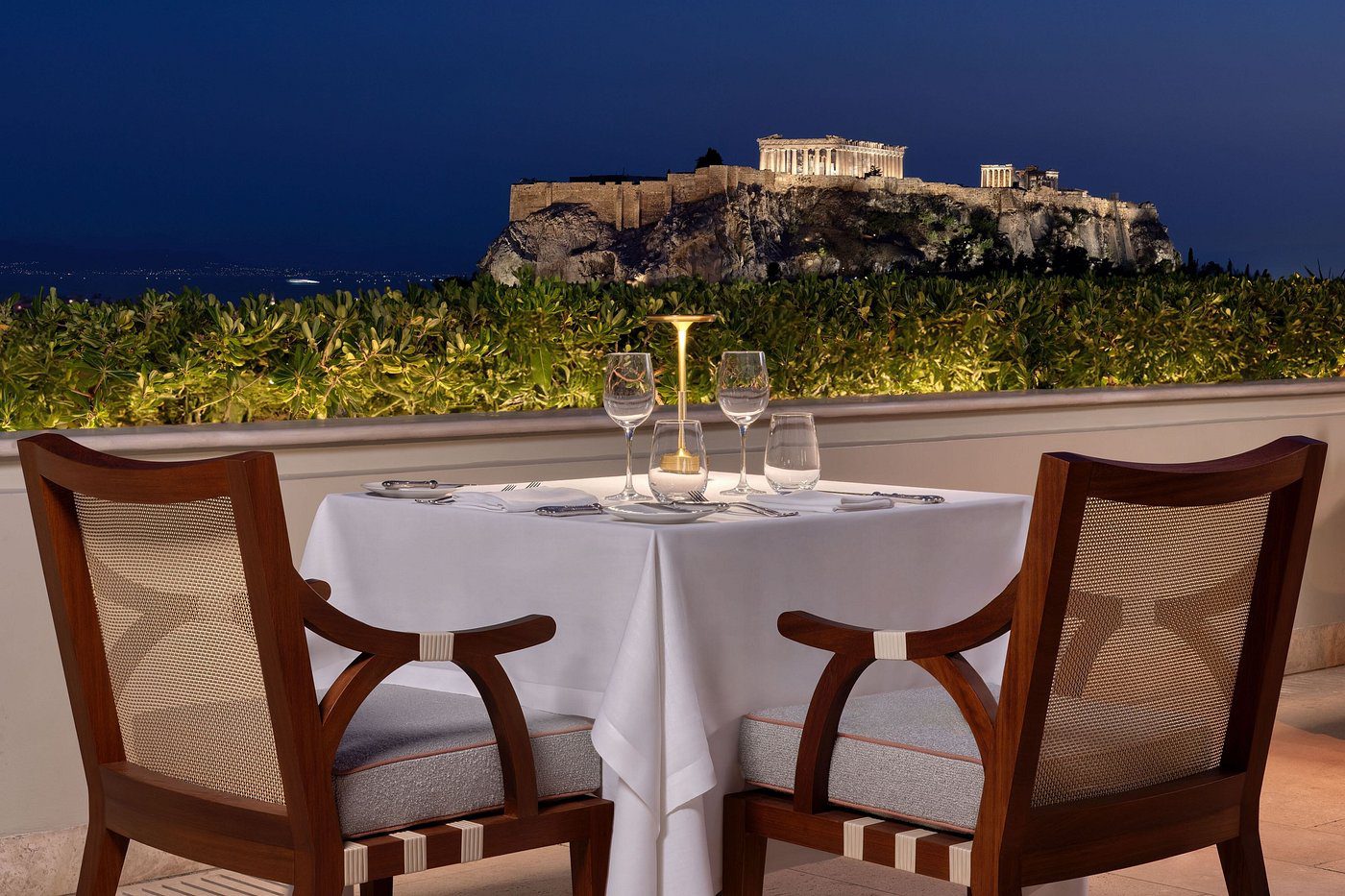 Elegant outdoor dinner setup with a view of the Acropolis at night.
