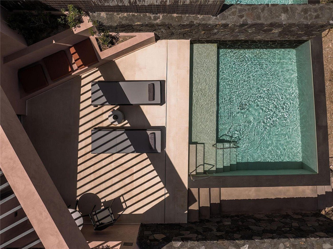 Top view of a modern poolside area with lounge chairs and shadows.