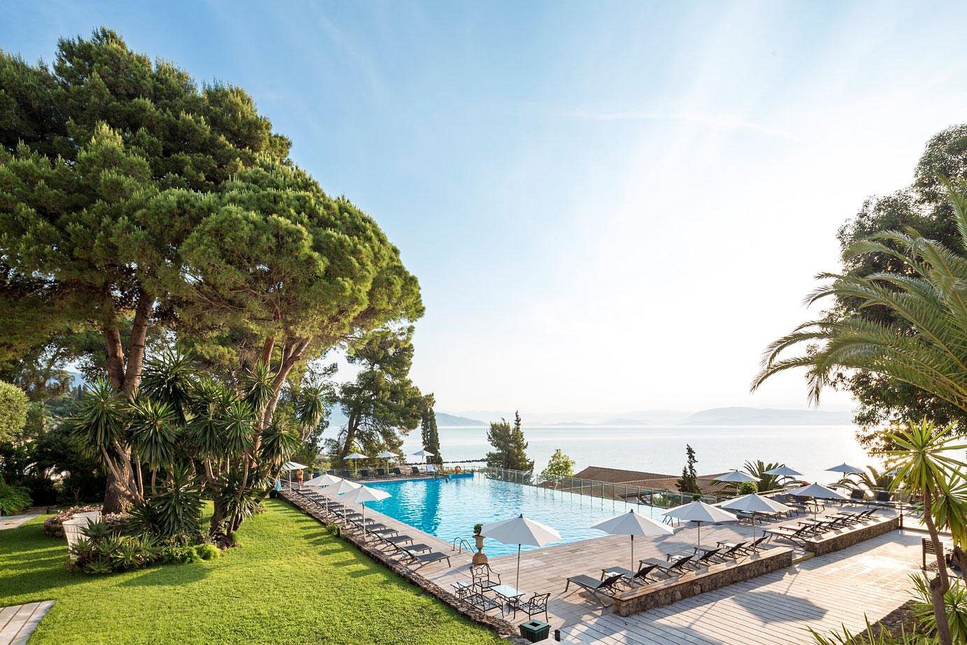 A serene outdoor pool surrounded by lounge chairs and greenery under a clear sky.
