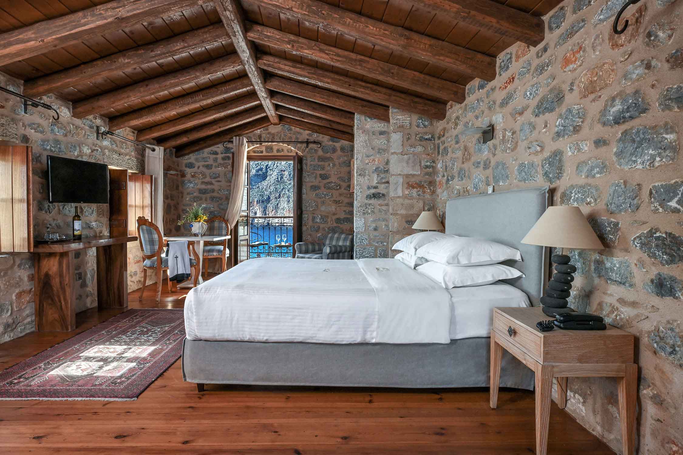 Cozy bedroom with stone walls and wooden ceiling beams.