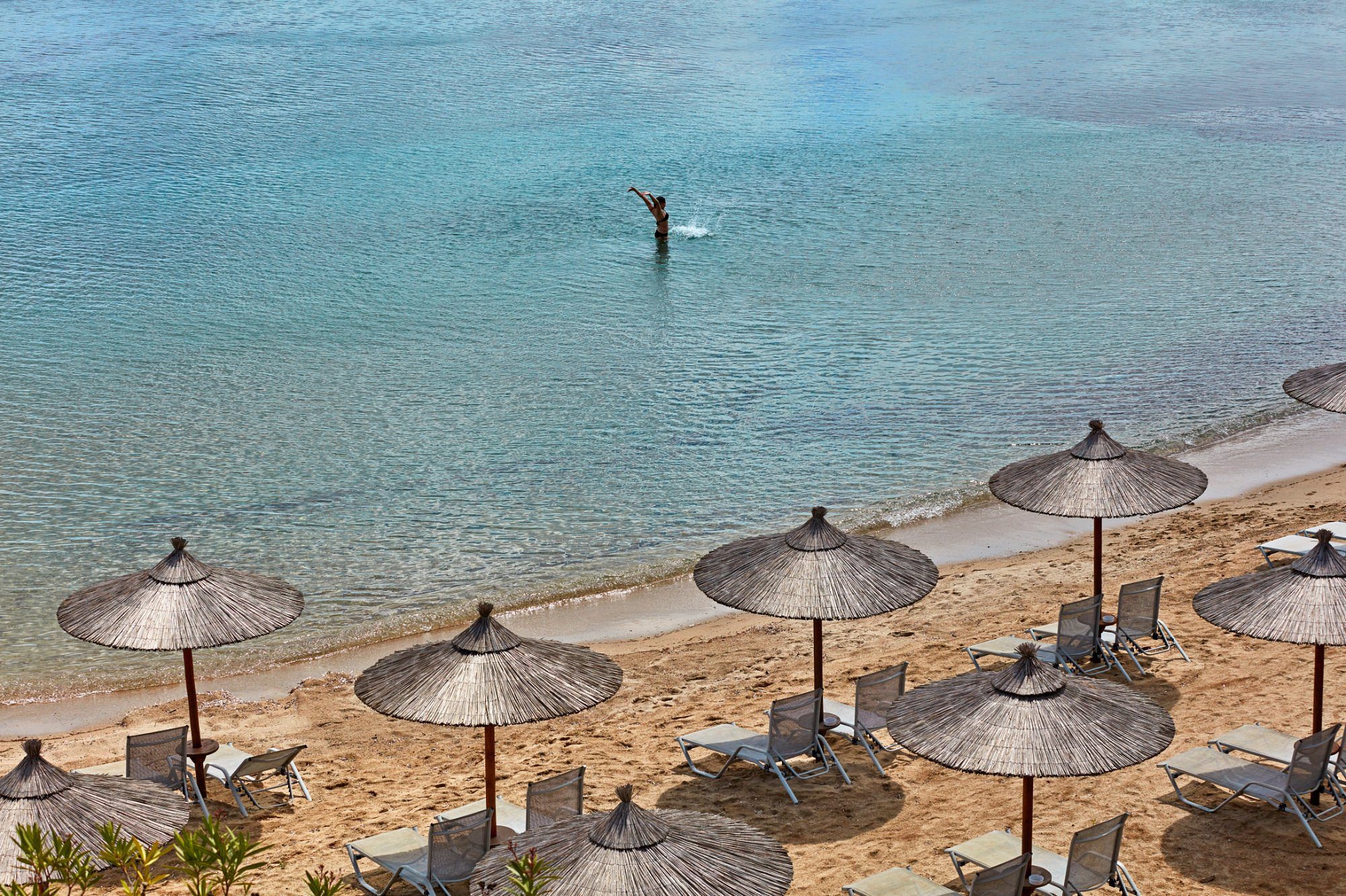 Thatched umbrellas line a sunny beach with clear turquoise water.