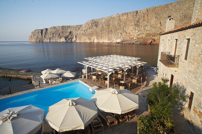 Seaside pool area with umbrellas and a rocky cliff backdrop.