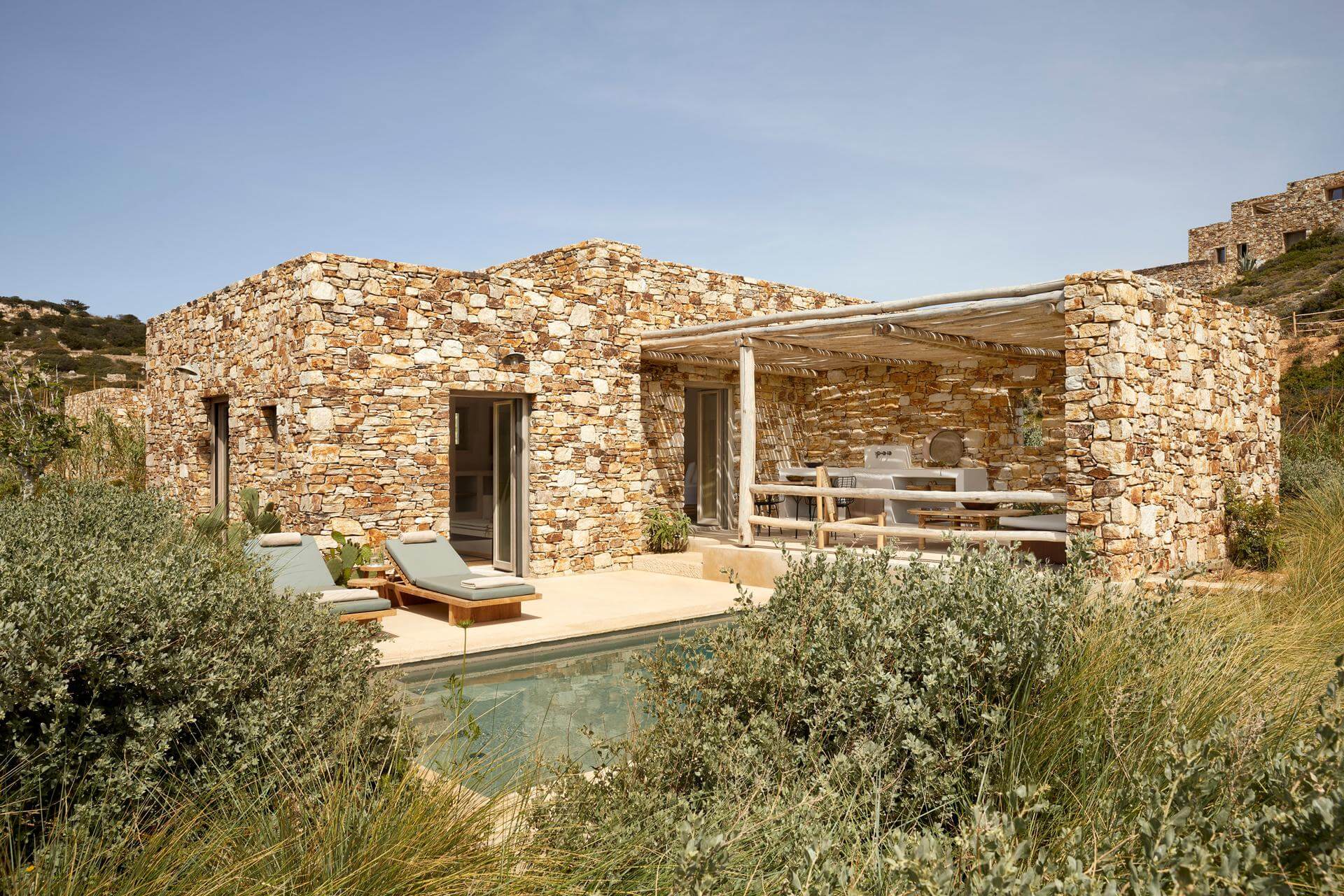 Rustic stone house with a small pool and outdoor seating under a clear sky.