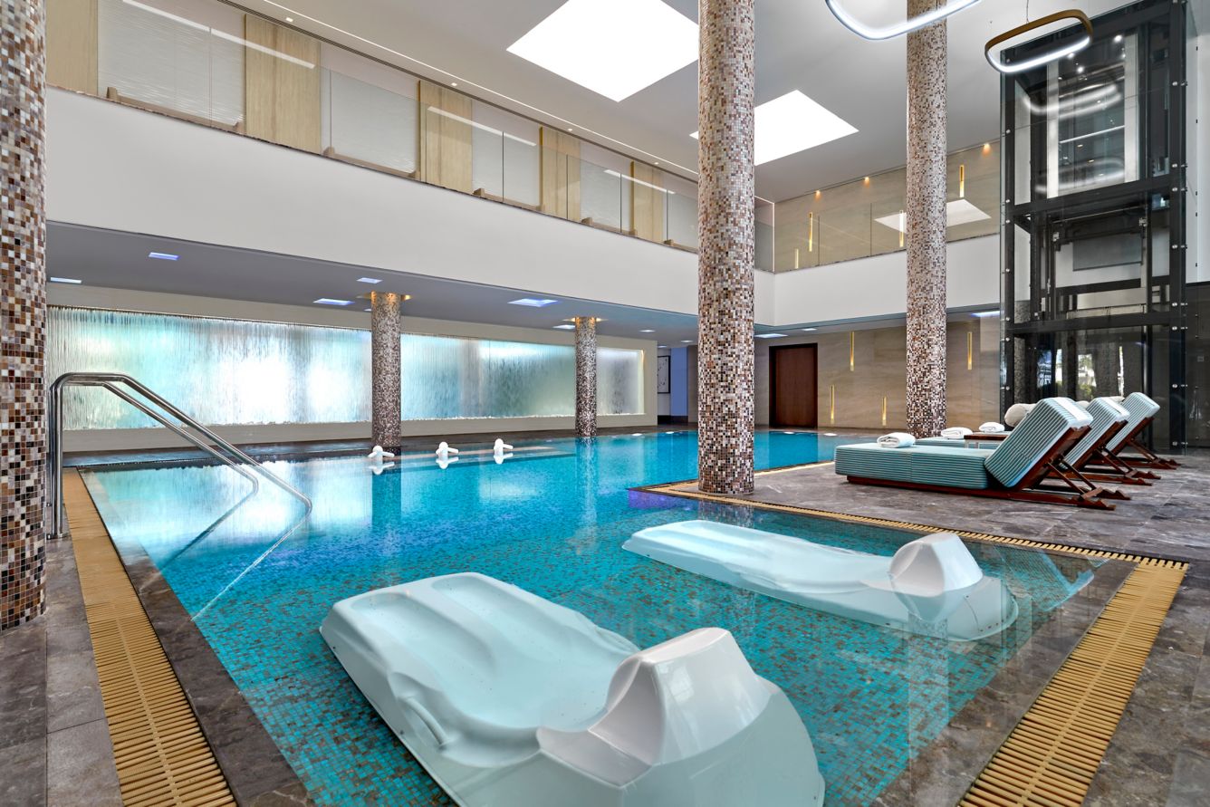 Luxurious indoor pool area with lounge chairs and stone pillars.