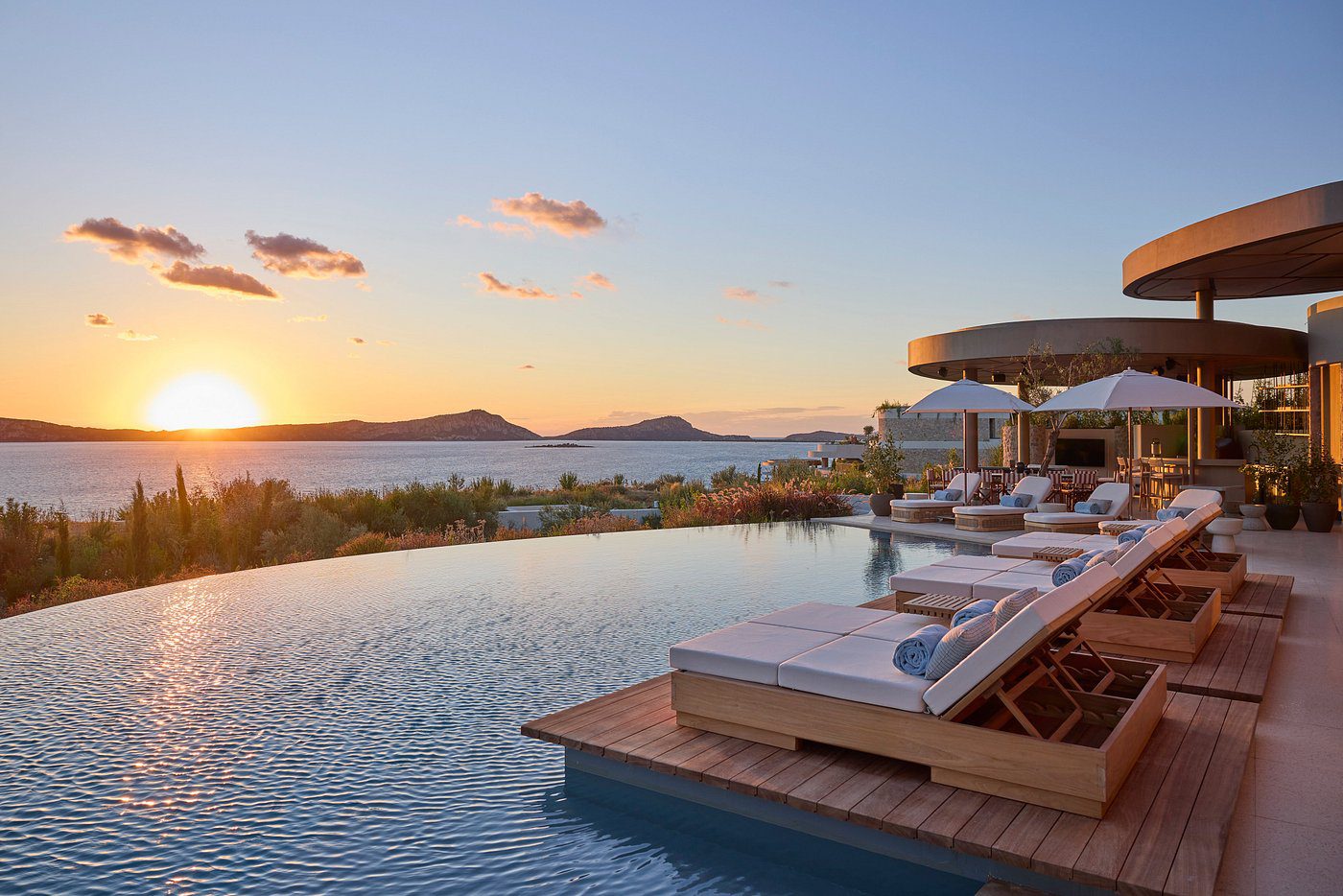 Sunset view over a luxurious infinity pool with loungers and a scenic horizon.