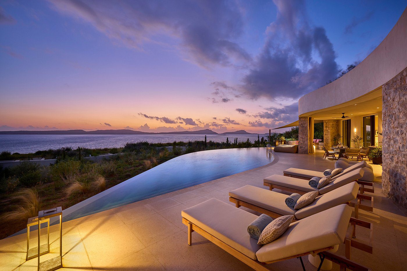 Infinity pool at sunset with lounge chairs and scenic views.