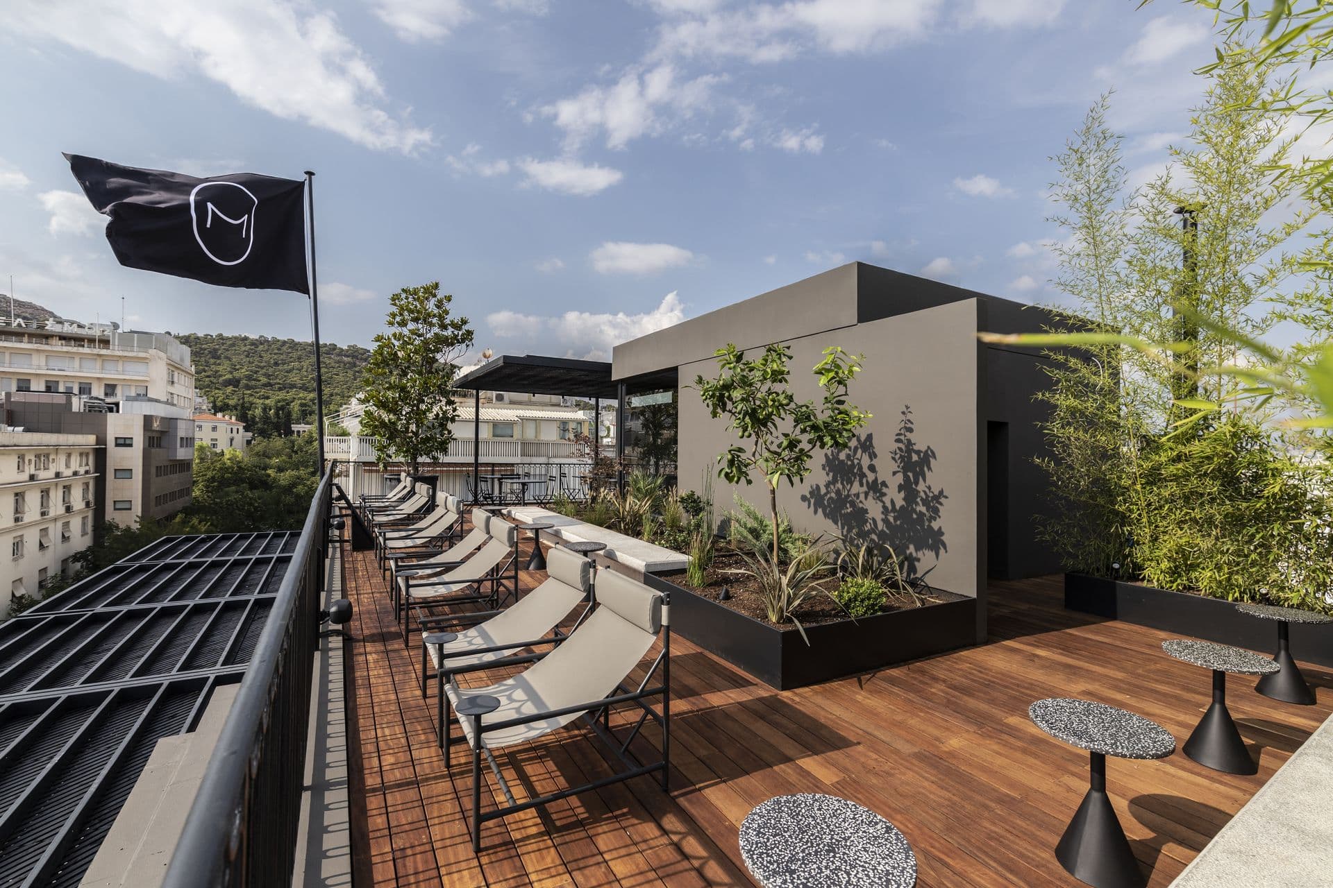 Modern rooftop terrace with lounge chairs and greenery under a blue sky.