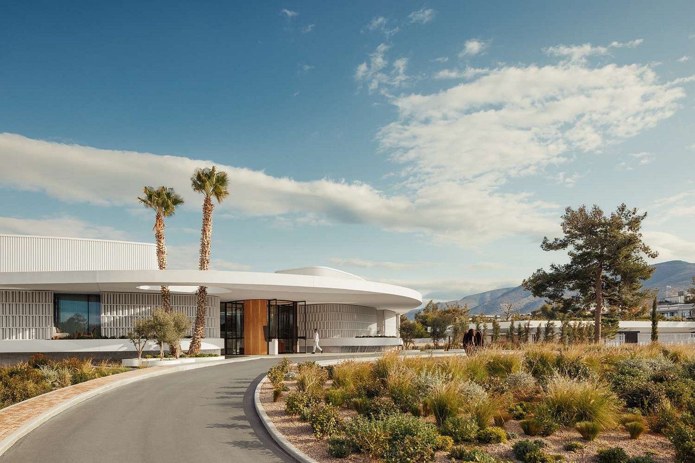 Modern building with curved design surrounded by desert landscaping and palm trees.