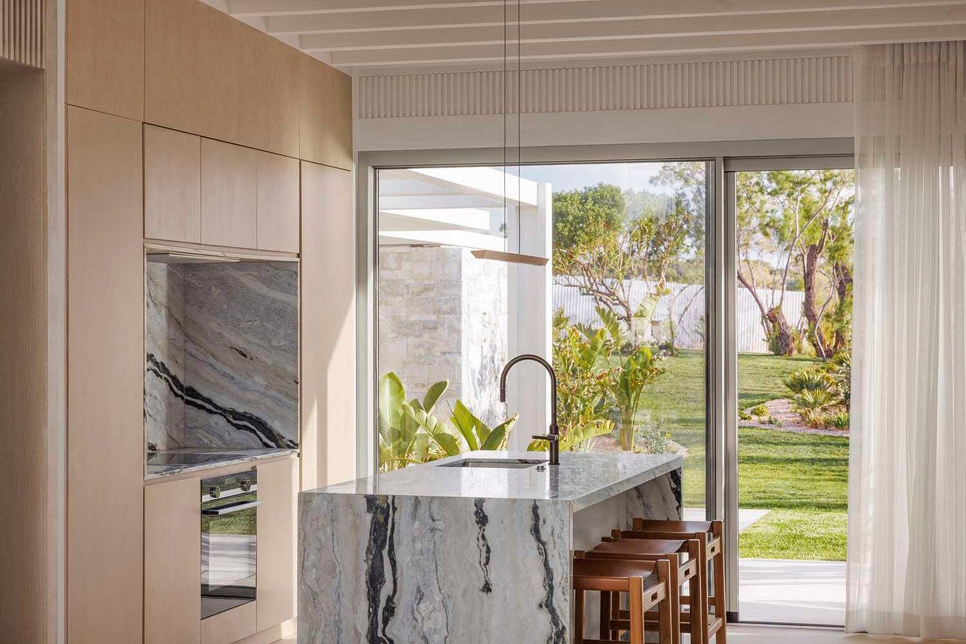 Modern kitchen with a marble island and garden view through large windows.